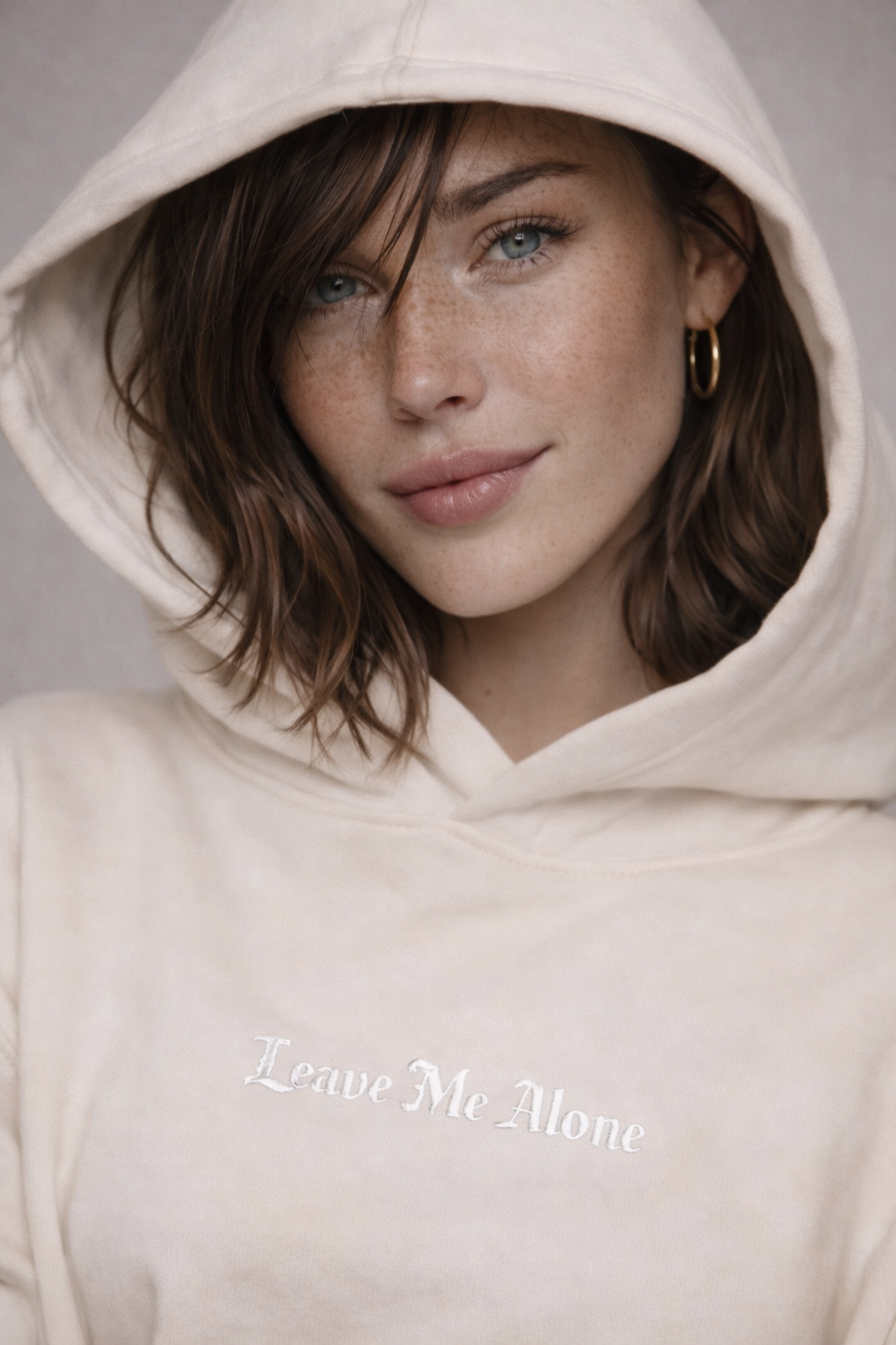female model hood up pose wearing oversized beige graphic streetwear hoodie minimal chest logo streetwear fashion