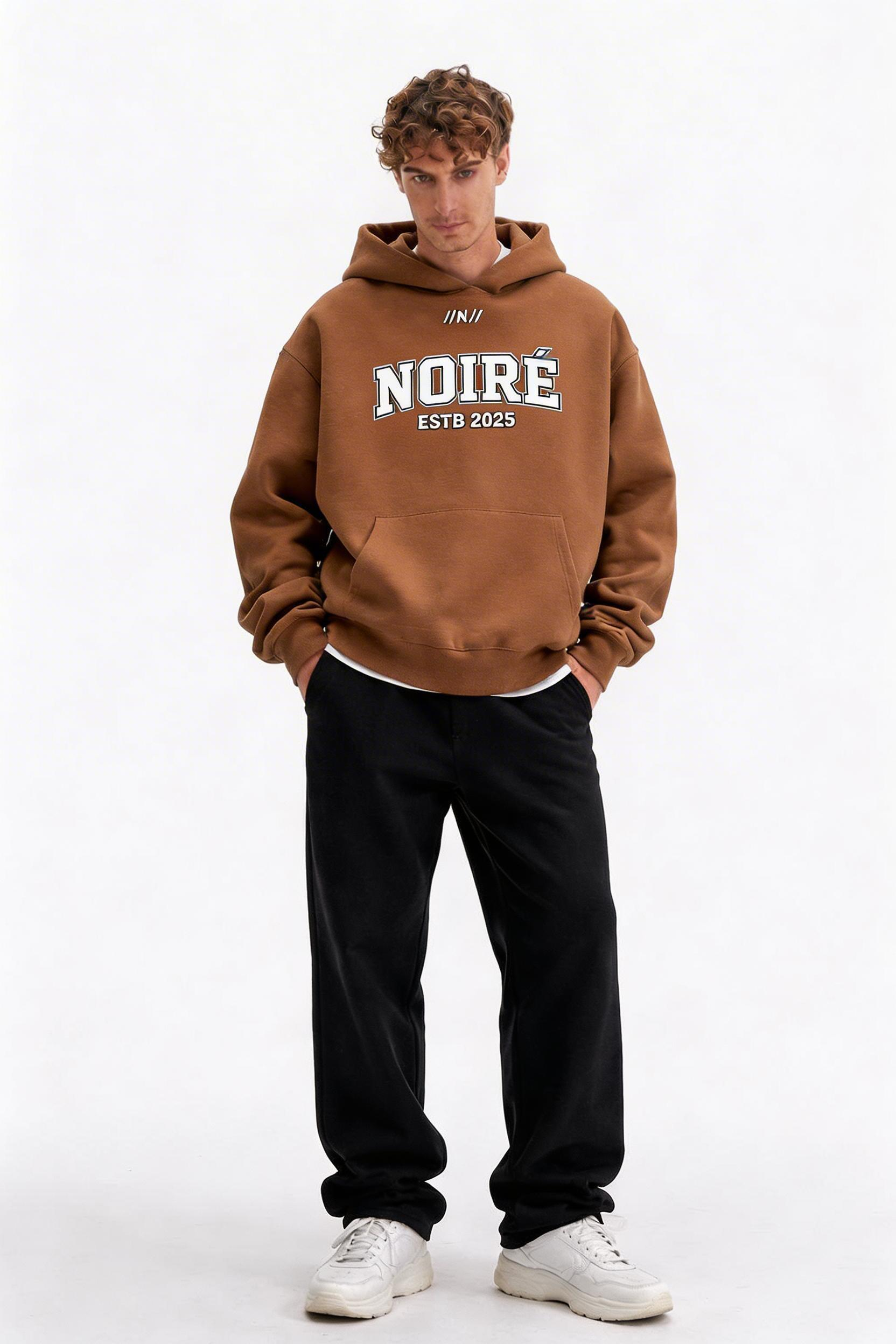 male model full body pose wearing oversized brown graphic streetwear hoodie noiré varsity logo design urban streetwear clothing