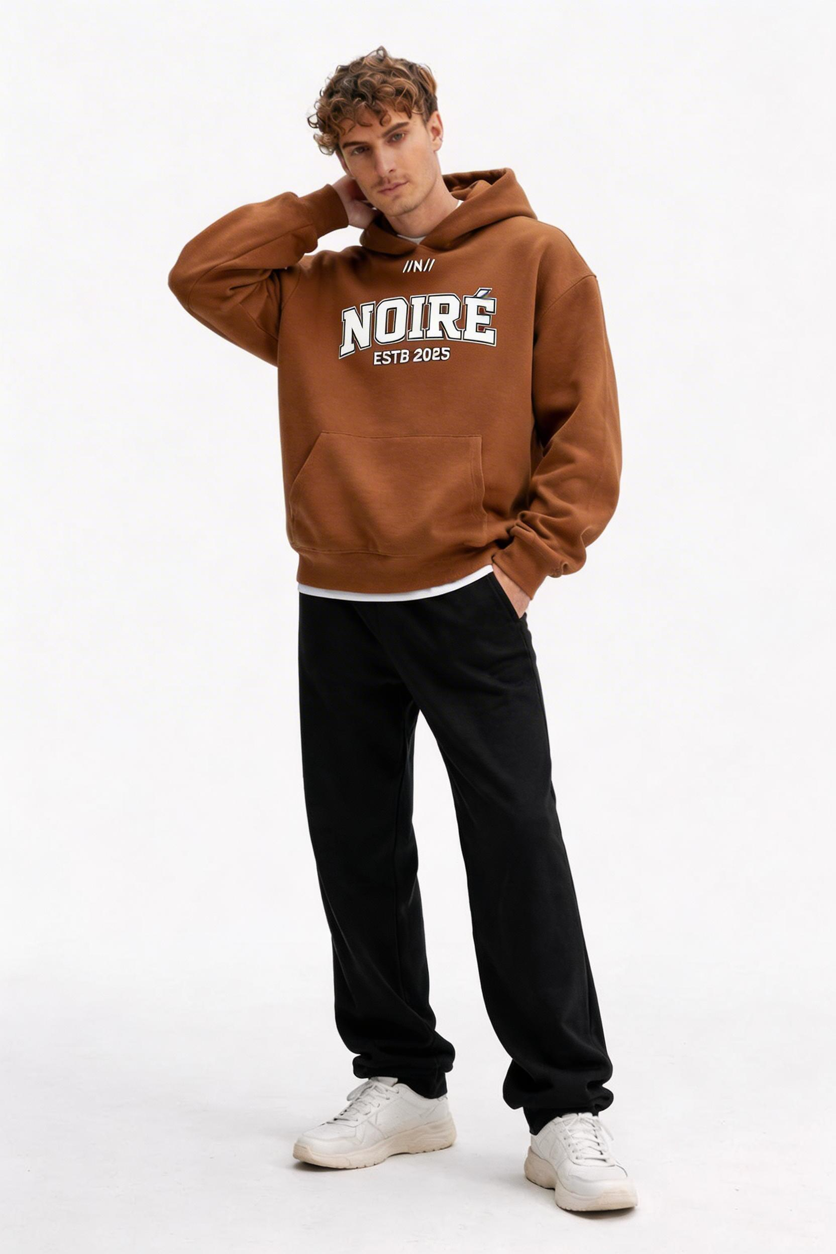male model relaxed pose wearing oversized brown graphic streetwear hoodie noiré varsity logo streetwear outfit
