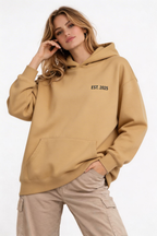 female model relaxed pose wearing oversized brown clean hoodie noiré est 2025 branding minimal streetwear fashion