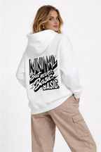 female model looking back pose wearing oversized white hoodie bold typography back print minimal but never basic streetwear fashion