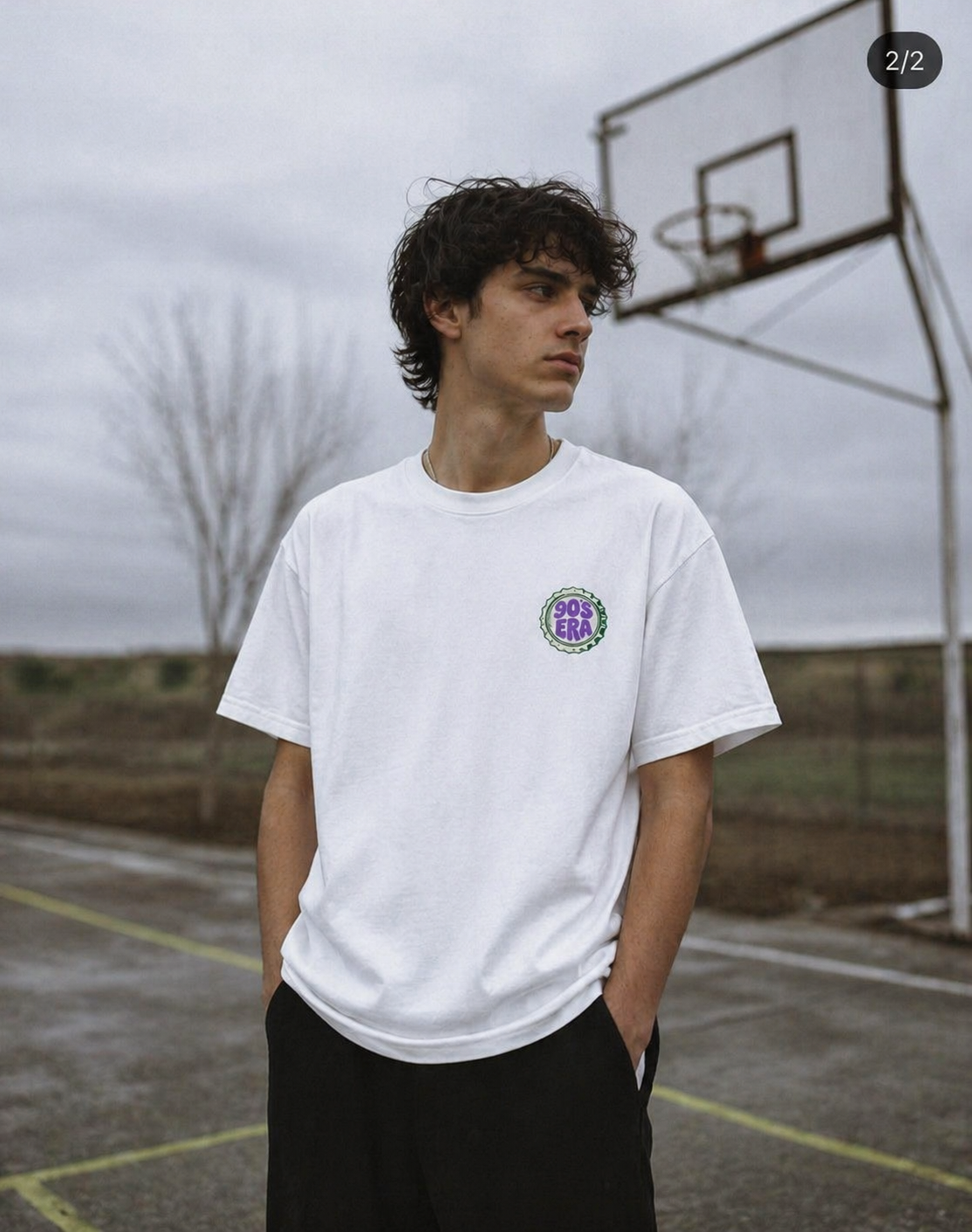 male model standing courtside wearing oversized white graphic t shirt 90s era chest logo urban streetwear outfit