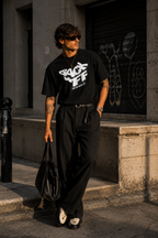 model standing side pose wearing relaxed fit black graphic t shirt back off statement print urban streetwear outfit