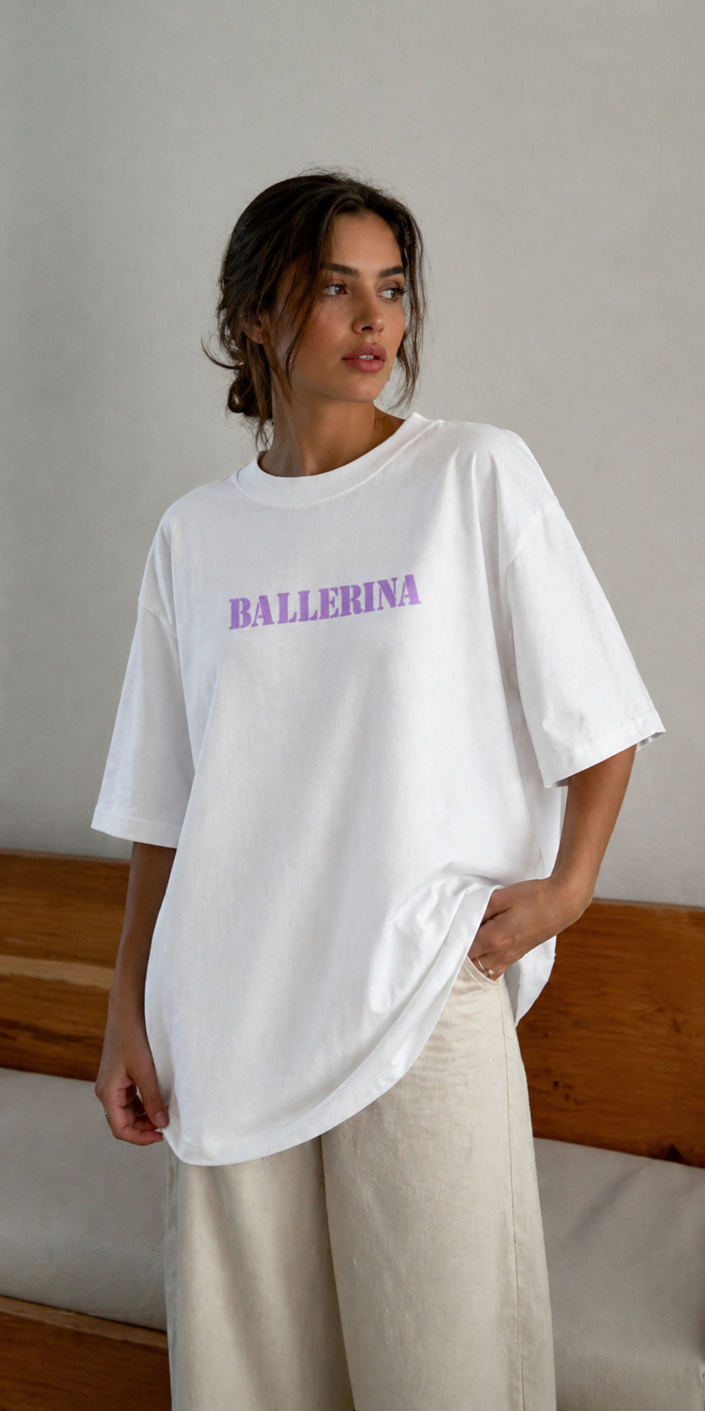 model posing indoors wearing oversized white ballerina graphic t-shirt with pastel purple text front print streetwear fashion