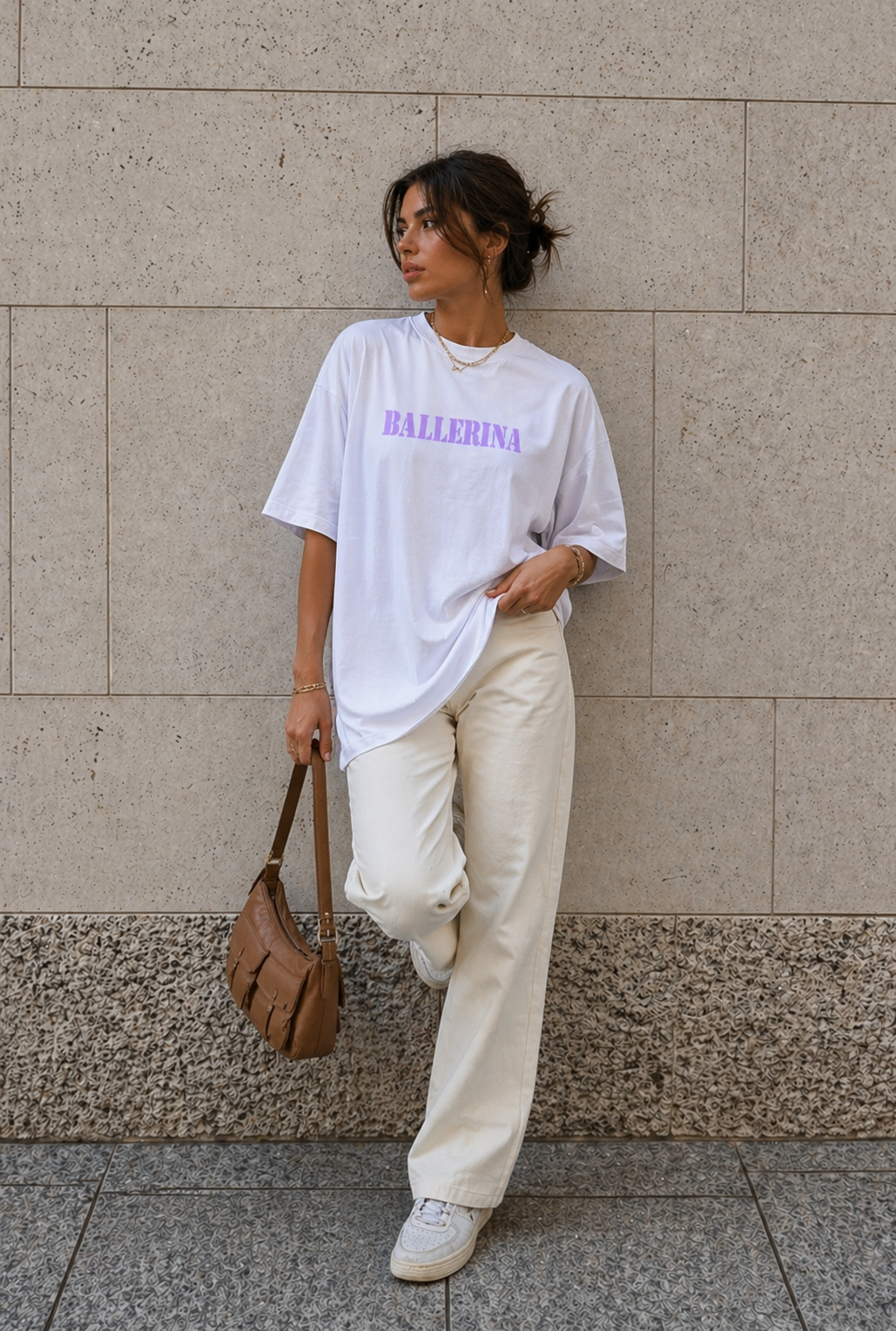 model standing against stone wall wearing oversized white ballerina graphic t-shirt cream wide leg pants urban streetwear outfit