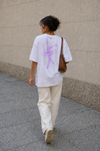 model walking away wearing oversized white ballerina graphic t-shirt with pastel purple back artwork urban streetwear outfit