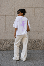 model posing against wall wearing oversized white ballerina graphic t-shirt cream pants and brown shoulder bag urban streetwear outfit