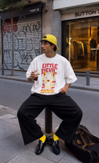 male model sitting on street bollard wearing oversized white graphic t shirt with little devil cartoon design and relaxed fit urban streetwear outfit