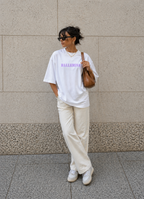 model posing against wall wearing oversized white ballerina graphic t-shirt cream pants and brown shoulder bag urban streetwear outfit