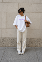 model standing wearing oversized white ballerina graphic t-shirt cream pants and brown shoulder bag urban streetwear outfit