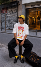 male model seated in city street wearing relaxed fit white oversized graphic t shirt with cartoon devil artwork urban streetwear