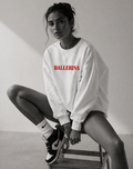 model sitting on chair wearing oversized white ballerina graphic sweatshirt with red statement text streetwear fashion