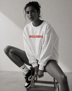 model sitting on chair wearing oversized white ballerina graphic sweatshirt with red statement text streetwear fashion