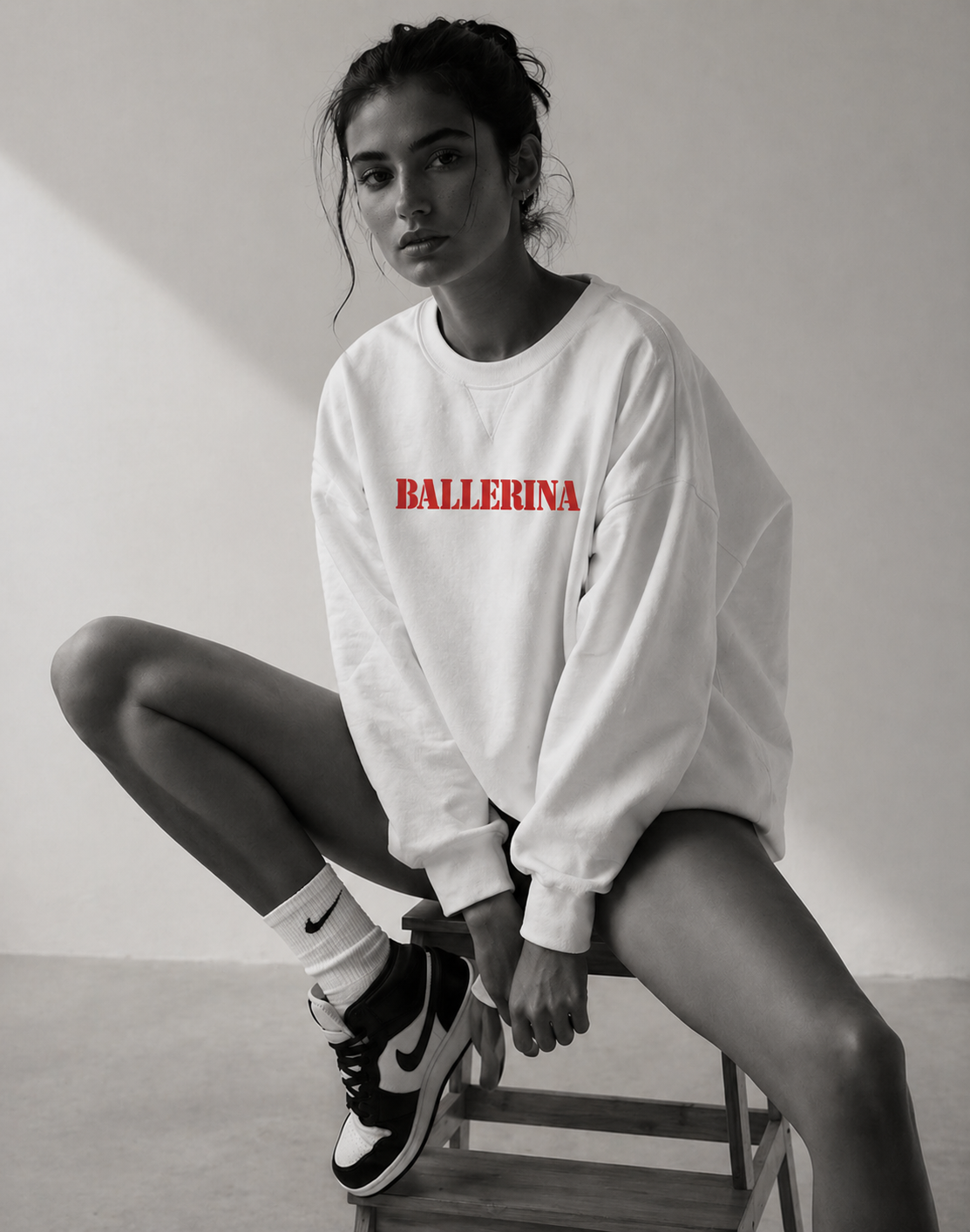 model sitting on chair wearing oversized white ballerina graphic sweatshirt with red statement text streetwear fashion