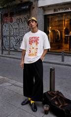 male model standing in street wearing oversized white graphic t shirt with little devil design and wide leg pants urban streetwear outfit