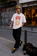 male model walking in city street wearing relaxed fit white graphic t shirt with little devil cartoon print urban streetwear fashion