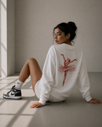 model seated back pose wearing oversized white ballerina sketch sweatshirt red back print graphic streetwear