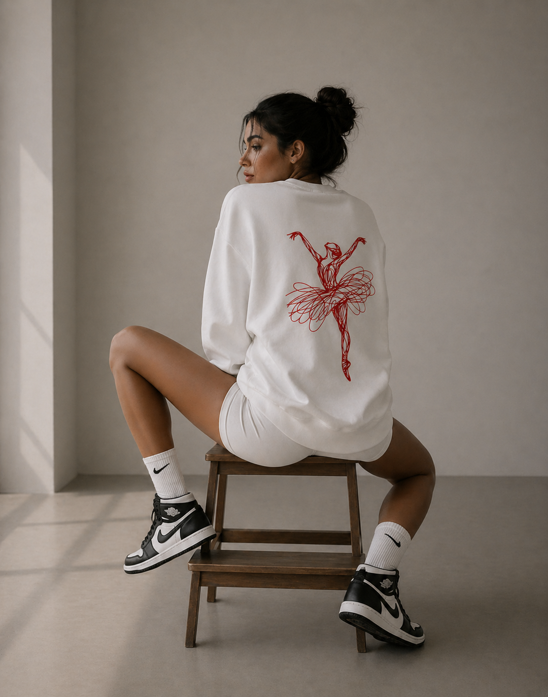 model seated on chair back pose wearing oversized white ballerina sweatshirt red back graphic streetwear fashion