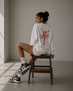model side seated on chair wearing oversized white ballerina sketch sweatshirt red back print graphic streetwear