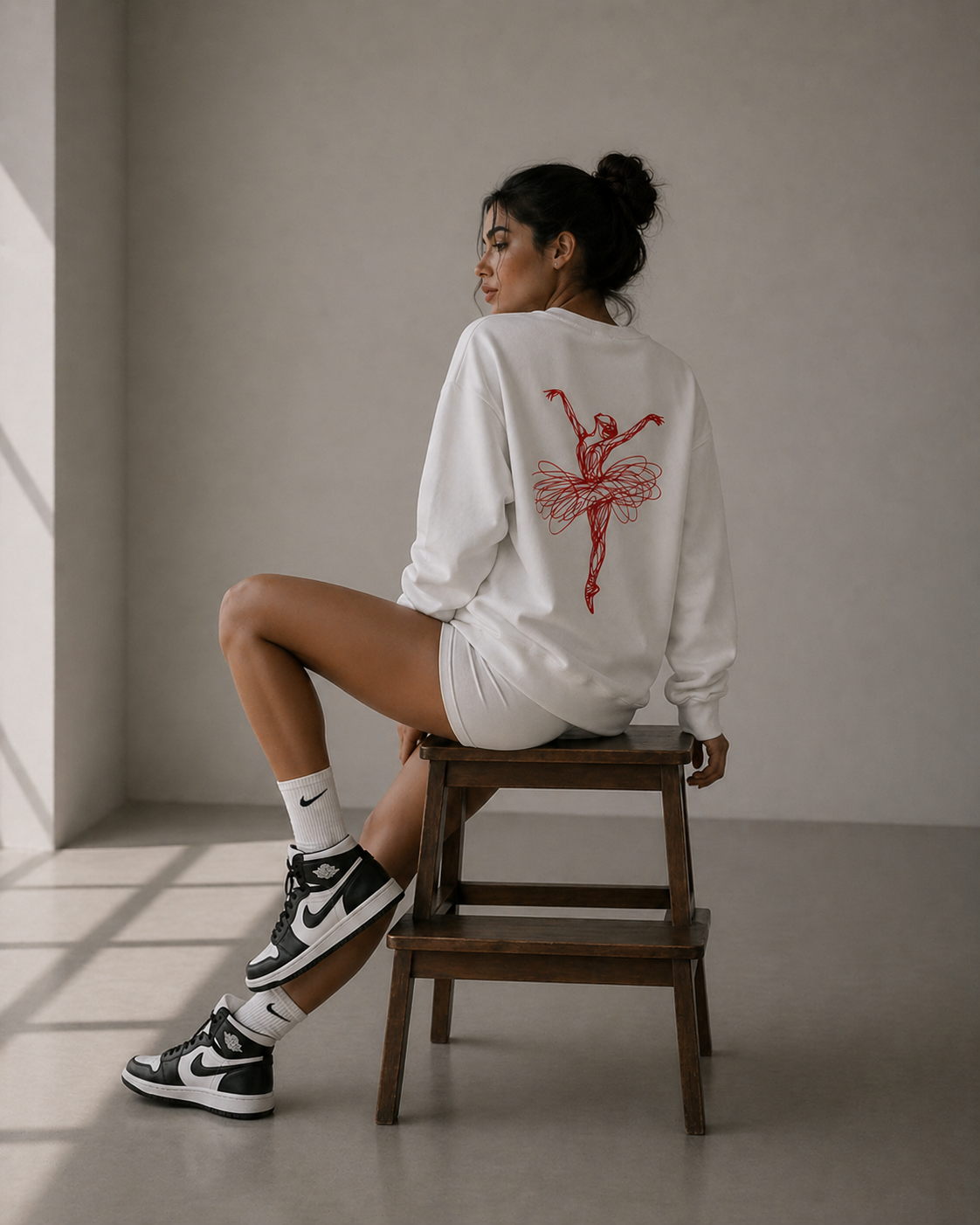 model side seated on chair wearing oversized white ballerina sketch sweatshirt red back print graphic streetwear