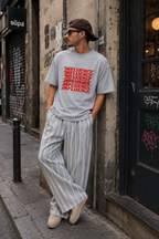 male model leaning against city wall wearing oversized heather gray graphic t shirt with red influence text artwork and relaxed fit graphic streetwear fashion