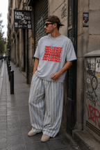 male model posing beside graffiti covered building wearing oversized gray graphic t shirt featuring influence typography design urban streetwear style