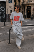 male model leaning on street rail wearing oversized sport gray graphic t shirt with bold red influence graphic and relaxed streetwear silhouette urban fashion