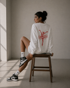model seated back view on wooden chair wearing oversized white ballerina graphic sweatshirt red ballerina design urban streetwear outfit