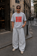 male model standing in city street wearing oversized gray graphic t shirt featuring red influence lettering graphic and casual urban streetwear outfit