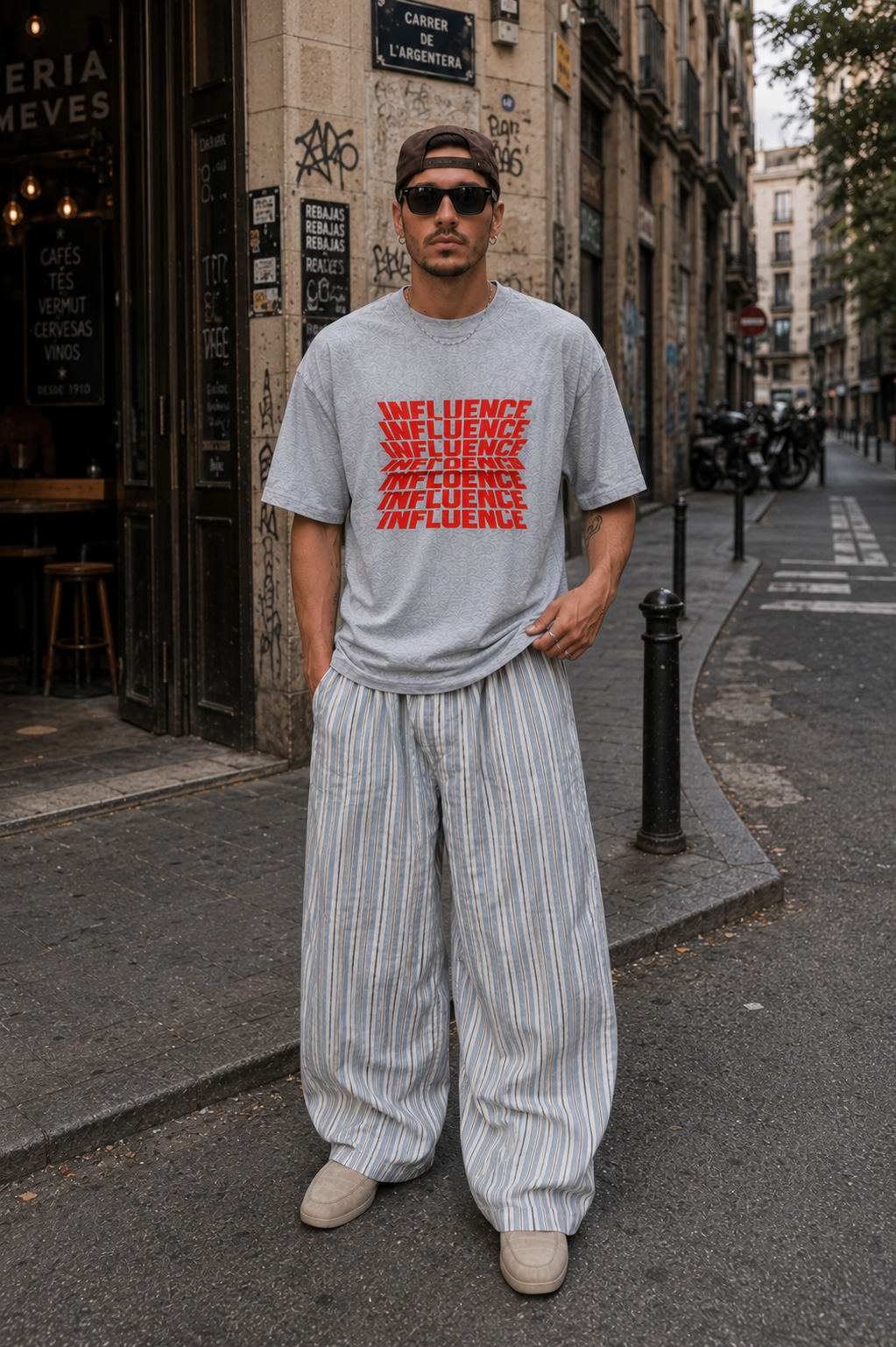 male model standing in city street wearing oversized gray graphic t shirt featuring red influence lettering graphic and casual urban streetwear outfit