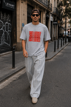 male model walking through urban street wearing oversized sport gray graphic t shirt with red influence typography design and relaxed streetwear fit graphic streetwear style
