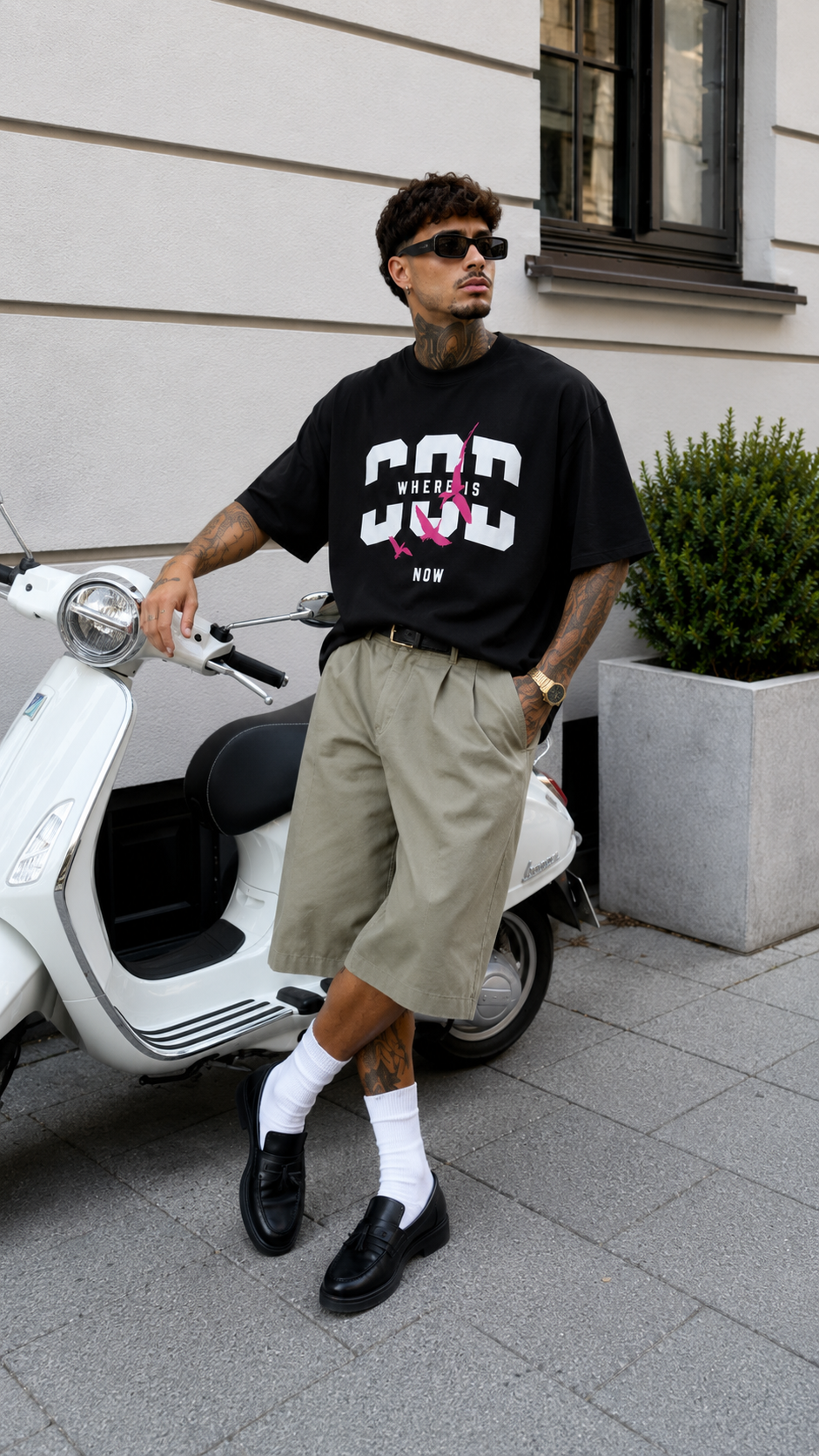 male model with sunglasses leaning on scooter wearing oversized black graphic t shirt with pink bird graphic streetwear fashion
