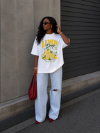 model adjusting hair wearing oversized white lemon drop graphic t shirt summer edition with relaxed fit light wash denim urban streetwear outfit