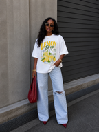 model front pose wearing oversized white lemon drop lemonade graphic t shirt with ripped light wash jeans and red heels streetwear fashion