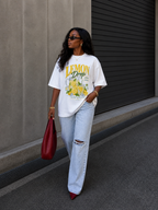 model walking view wearing oversized white lemon drop summer graphic t shirt relaxed fit with light wash distressed jeans urban streetwear outfit