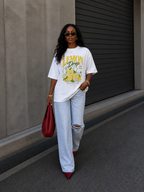 model walking front view wearing oversized white lemon drop graphic t shirt summer edition with wide leg ripped jeans streetwear fashion