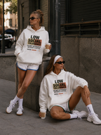 streetwear editorial photo of two female models in oversized white hoodies with graphic typography print relaxing in city setting urban fashion aesthetic