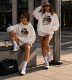 two women posing in oversized cream graphic hoodies with low social tolerance slogan modern streetwear fashion editorial