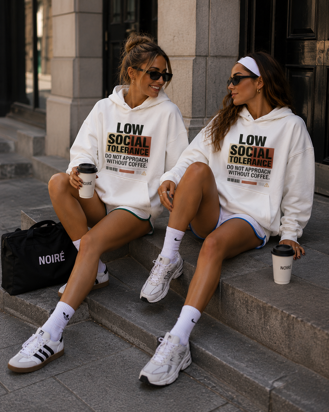 female models smiling while wearing oversized white graphic hoodies with low social tolerance design casual streetwear fashion editorial outdoors