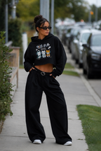 model side pose wearing cropped black anime graphic hoodie relaxed wide leg pants streetwear fashion