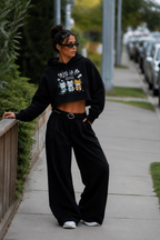 model leaning on railing wearing black cropped graphic hoodie wide leg black pants urban streetwear outfit