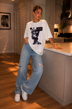 woman standing by kitchen island wearing oversized white graphic t shirt beyond average futuristic artwork streetwear fashion