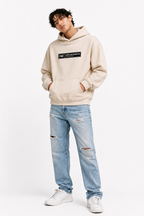 male model casual front pose wearing oversized beige graphic streetwear hoodie minimal chest logo urban streetwear outfit