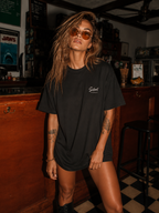 woman posing in vintage bar wearing relaxed fit black oversized graphic t shirt with minimalist chest logo graphic streetwear outfit