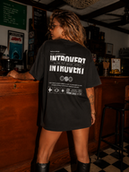 woman leaning on bar wearing oversized black graphic t shirt with large Introvert typography back design graphic streetwear outfit