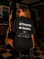 woman kneeling beside pool table wearing oversized black graphic t shirt featuring bold Introvert back graphic urban streetwear fashion