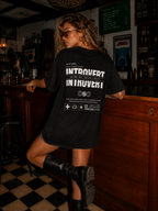 woman standing near bar counter wearing oversized black graphic t shirt with Introvert statement artwork on back graphic streetwear apparel