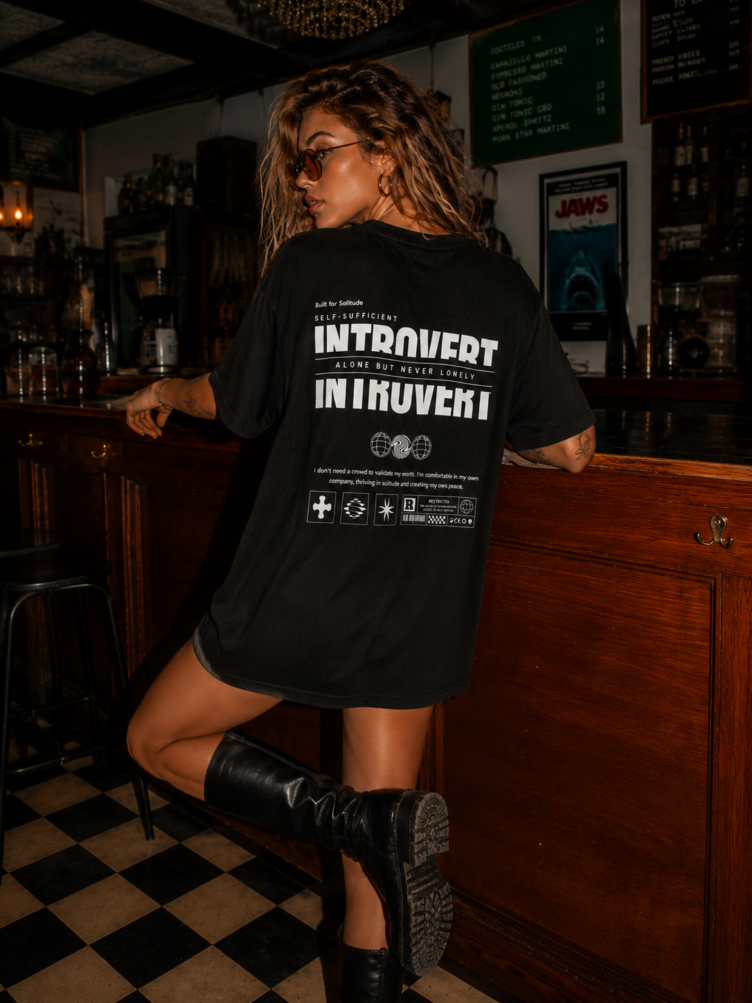 woman standing near bar counter wearing oversized black graphic t shirt with Introvert statement artwork on back graphic streetwear apparel
