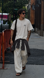 male model walking through city street wearing oversized off white graphic t shirt with small chest typography print relaxed fit urban streetwear outfit