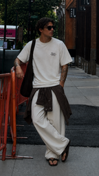 male model leaning on street barrier wearing oversized off white graphic t shirt with small front statement design urban streetwear look